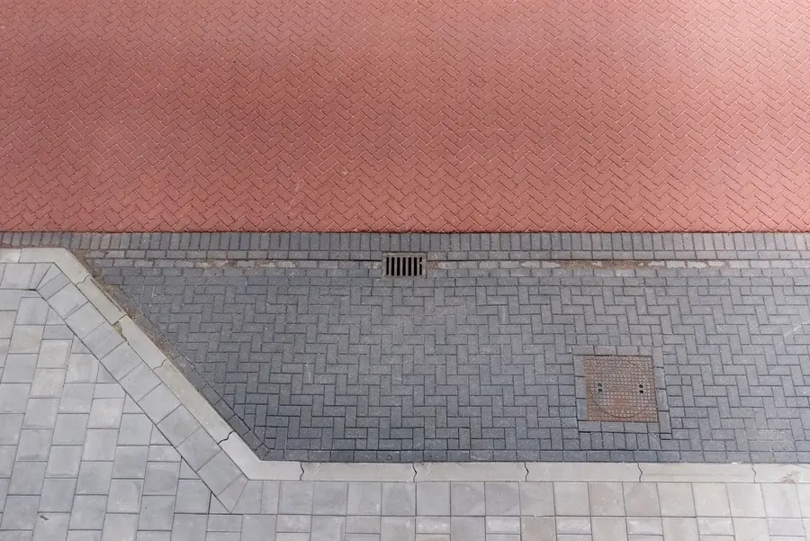 Paved surface meeting a kerb edge with a drainage gully, showing where driveway run-off is caught before the road