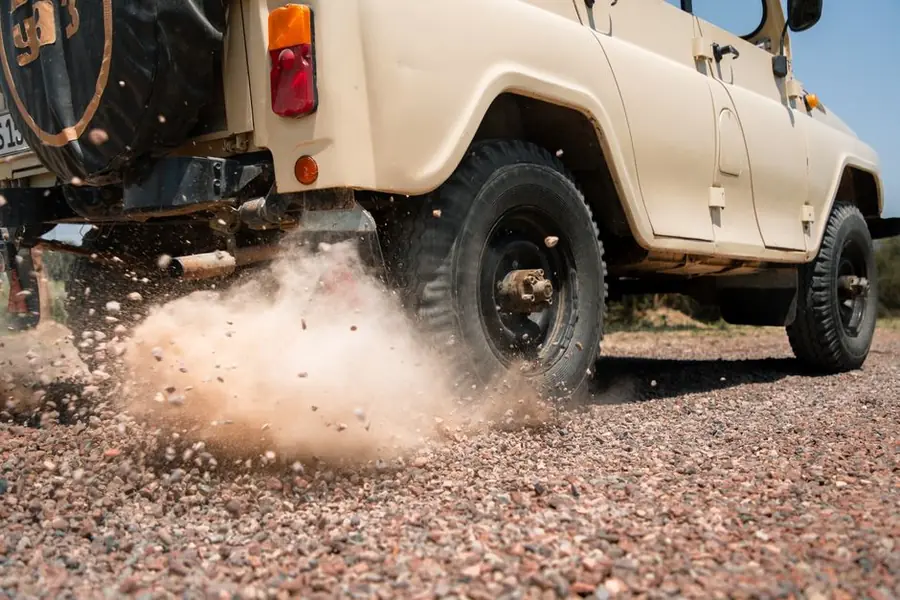 Car wheel spinning on loose gravel and throwing stones outwards