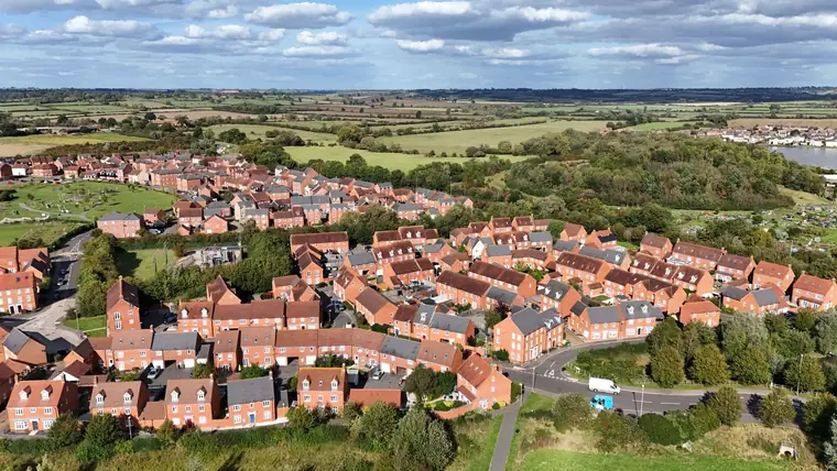 Aerial view of a modern red-brick new-build housing estate on the edge of open countryside, like the developments on the Swindon side of Royal Wootton Bassett