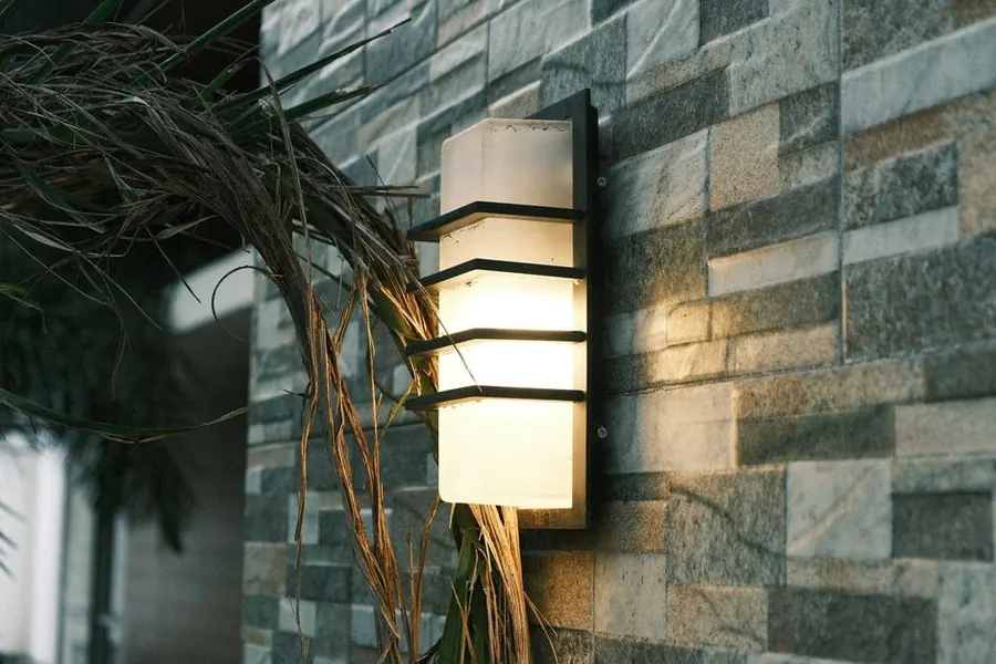 Outdoor wall lantern lighting a stone wall and planting beside a driveway