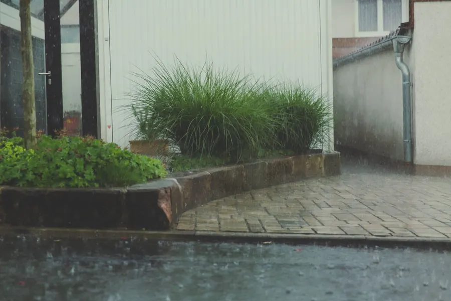 Heavy rain running off block paving beside a brick edging and a downpipe, the drainage and edge upkeep behind a Swindon driveway's running costs