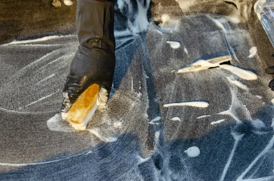 Gloved hand scrubbing a stain off a hard surface with detergent, the low-cost stain treatment a Swindon resin driveway occasionally needs