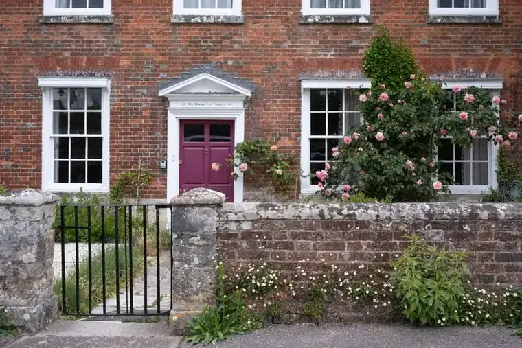 Traditional English brick house behind a low stone boundary wall and iron gate, the kind of frontage altered for a new driveway