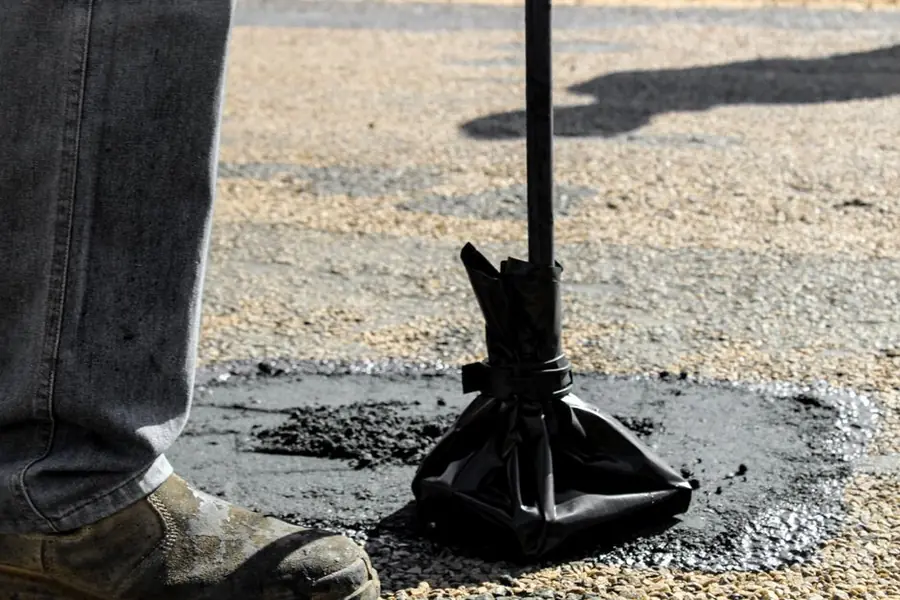 Hot asphalt being worked into a repair, the resurfacing cost that dominates a tarmac driveway's twenty year budget